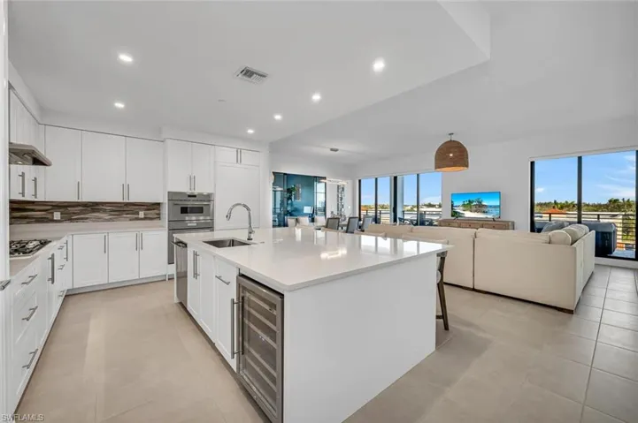 Kitchen featuring white cabinetry, sink, wine cooler, decorative backsplash, and a kitchen island with sink