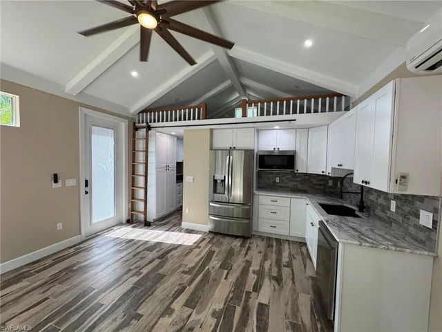 Kitchen with stainless steel appliances, sink, an AC wall unit, white cabinets, and vaulted ceiling with beams