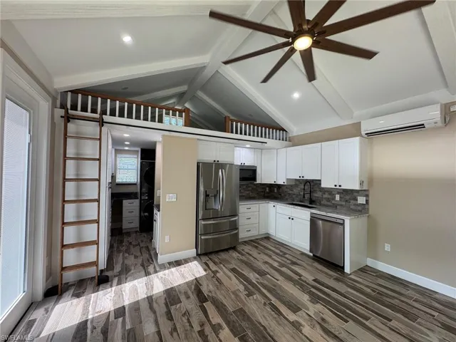 Kitchen featuring a wall mounted air conditioner, appliances with stainless steel finishes, dark wood-type flooring, sink, and vaulted ceiling with beams