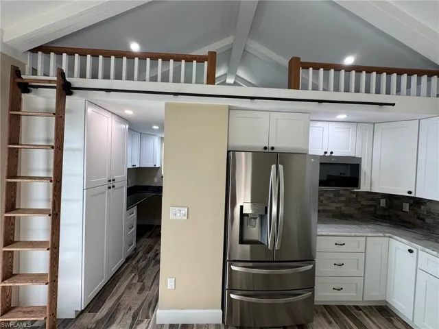 Kitchen with appliances with stainless steel finishes, lofted ceiling with beams, white cabinetry, and dark hardwood / wood-style flooring