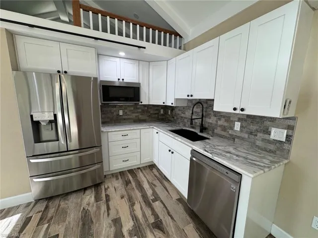Kitchen with appliances with stainless steel finishes, light stone counters, sink, white cabinets, and dark hardwood / wood-style floors