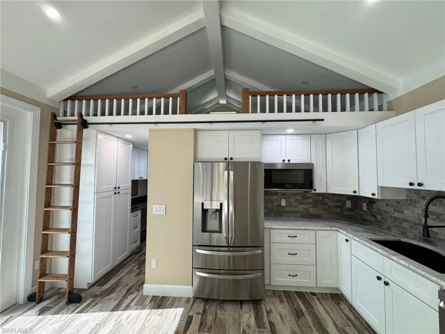 Kitchen with sink, dark wood-type flooring, stainless steel appliances, lofted ceiling with beams, and white cabinets