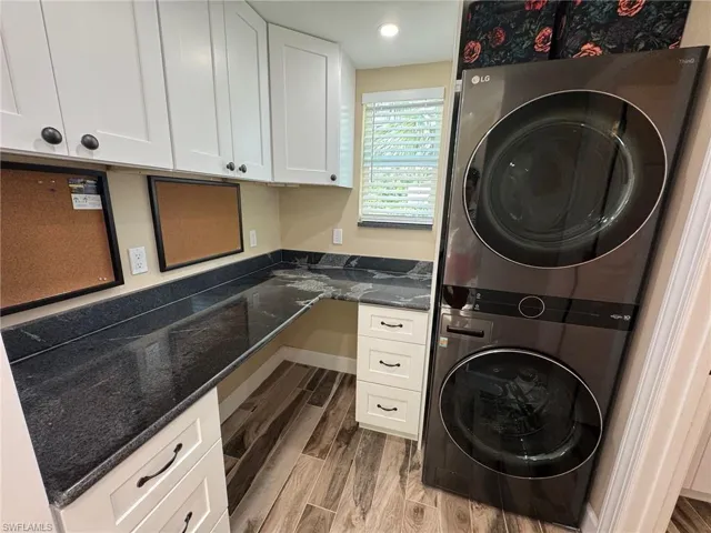 Washroom featuring hardwood / wood-style floors, cabinets, and stacked washer / dryer