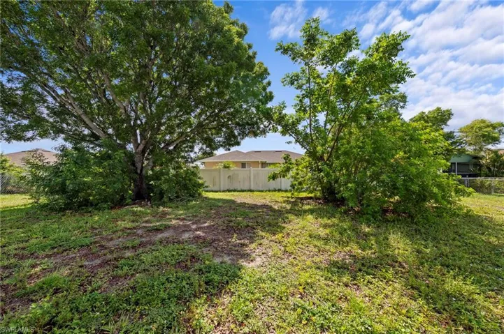 Expansive open lot featuring mature trees and a partial privacy fence