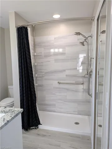 Shower with light-toned rectangular tile surround, white shower pan, dual shower heads, and an integrated grab bar