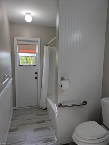 Bathroom featuring wood-finish tile flooring, beadboard wainscoting, and a full-size bathtub with shower