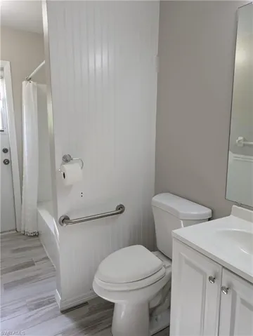 Bathroom featuring wood-look tile flooring, a white vanity with integrated sink, and white beadboard wall paneling