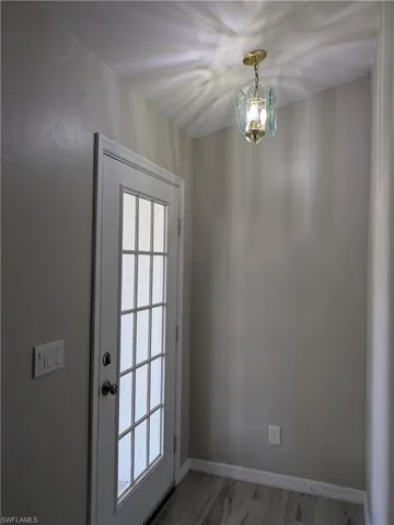 Entryway featuring a white paneled door with glass inserts, overhead brass and glass lighting fixture, light gray wall finish, and wood-finish flooring