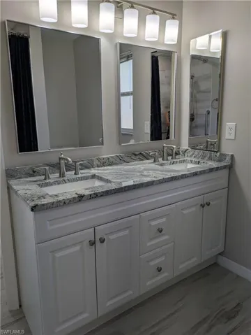 Dual vanity with white cabinetry and integrated sinks, complemented by a speckled countertop and wood-finish flooring