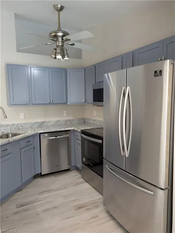 Modern kitchen featuring blue shaker-style cabinetry, light-toned countertops, stainless steel appliances, and wood-finish flooring