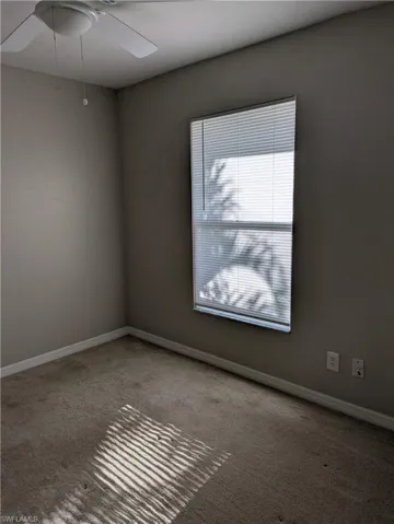 Neutral-toned room featuring a single window with blinds, a ceiling fan, and carpeted flooring
