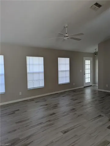 Spacious interior featuring wood-finish flooring, neutral paint palette, multiple windows with blinds, a ceiling fan, and a paneled door