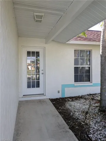 Front entry featuring a white paneled door with multiple glass lites, an overhead light fixture, a concrete walkway, and textured exterior walls