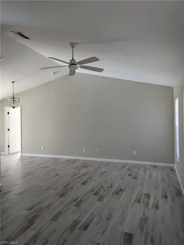Spacious room featuring vaulted ceilings, wood-finish flooring, a contemporary ceiling fan, and neutral wall tones