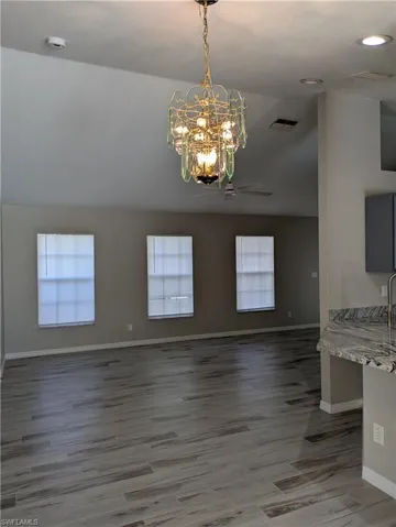 Vaulted ceiling with an ornate chandelier, wood-finish flooring, three large windows, a ceiling fan, and a granite countertop