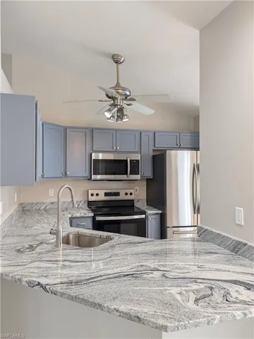 Kitchen featuring blue cabinetry, stainless steel appliances, a ceiling fan, and a light gray countertop with a built-in sink and gooseneck faucet