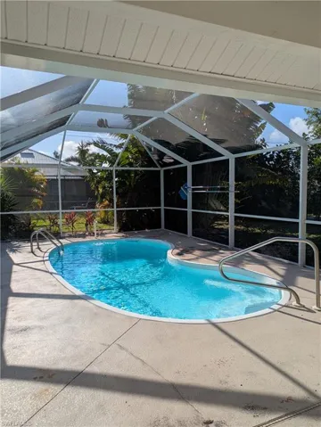 Screened-in pool area featuring a freeform swimming pool with integrated steps, concrete decking, and a full enclosure with white aluminum framing