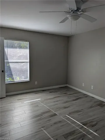 Neutral-toned room featuring wood-look tile flooring, a window with horizontal blinds, and a ceiling fan with integrated lighting