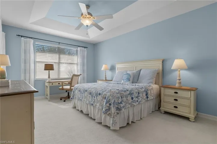 Bright and airy primary bedroom with tray ceiling and ceiling fan.