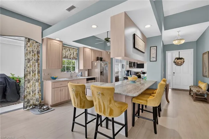 Kitchen featuring light wood-finish cabinetry, light stone-finish countertops, stainless steel appliances, and an expansive breakfast bar with seating