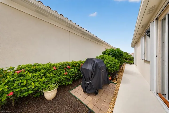 Exterior side yard featuring a stucco wall, mature shrubbery with pink blooms, and a paved walkway