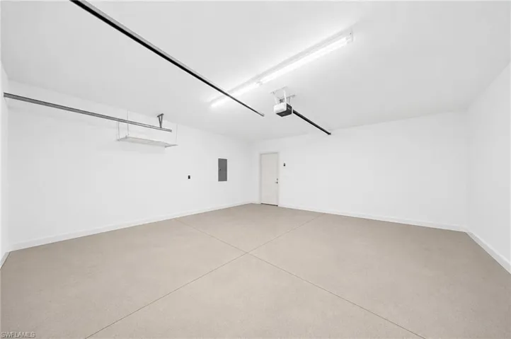 Spacious garage featuring a light-colored concrete floor, pristine white walls, and overhead fluorescent lighting