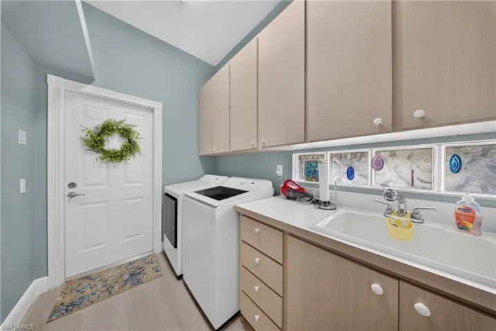 Functional utility space featuring light wood-finish cabinetry, a white countertop with an integrated sink, and light wood-finish flooring