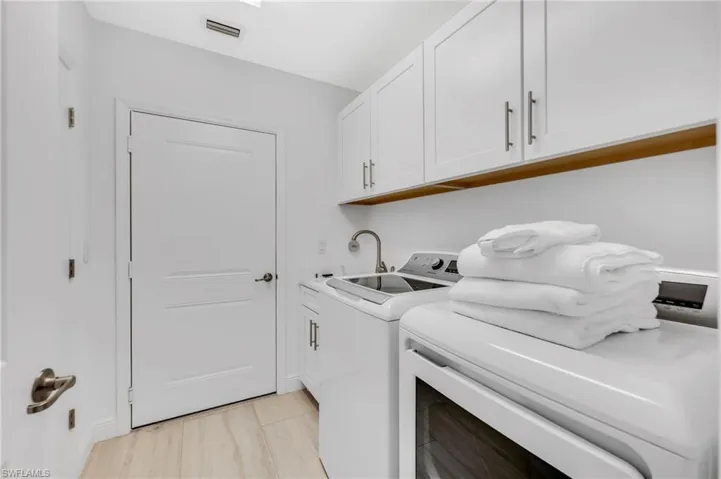 Dedicated laundry area featuring white shaker-style cabinetry, a built-in utility sink with a brushed nickel faucet, and wood-finish flooring