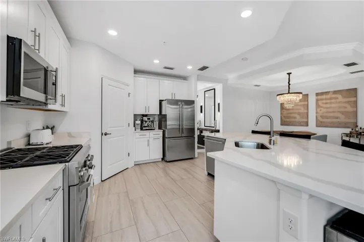 Modern kitchen featuring white cabinetry, stainless steel appliances, light wood-finish flooring, a large island with an undermount sink, and recessed lighting