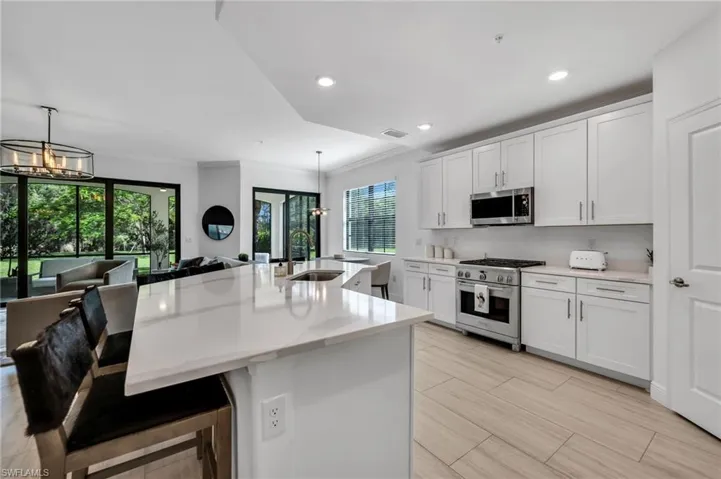 Expansive kitchen featuring a large island with a waterfall countertop, white shaker cabinetry, stainless steel appliances, and light wood-finish flooring