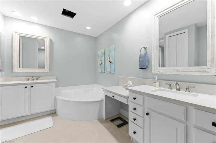 Full bathroom featuring two vanities, a bath, light tile patterned flooring, and recessed lighting