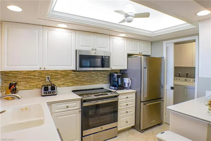 Kitchen with stainless steel appliances, sink, light tile patterned floors, separate washer and dryer, and white cabinetry