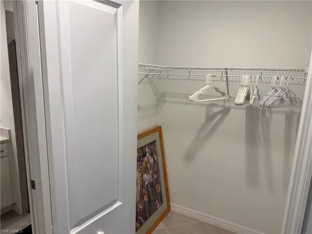 Walk-in closet featuring white paneled door entry, neutral-tone tile flooring, and integrated white wire shelving
