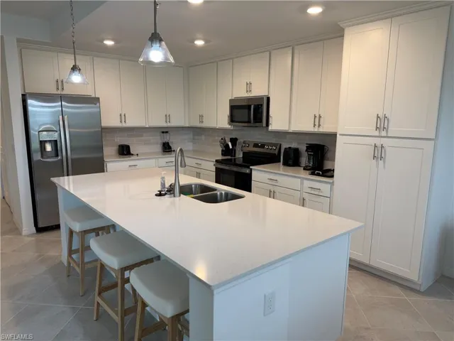 Kitchen featuring white cabinetry, quartz countertops, a central island with a double-basin stainless steel sink, tile backsplash, and recessed lighting