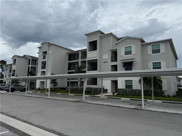 Multi-story residential building featuring a stucco exterior, decorative window shutters, integrated balconies, and a covered parking structure