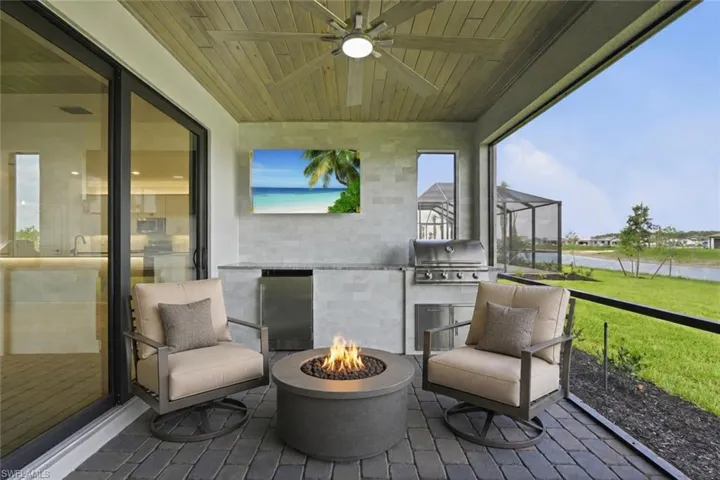 Covered outdoor living space featuring paver flooring, a wood-finish ceiling with a ceiling fan, and a built-in outdoor kitchen with a grill and stainless steel undercounter refrigerator