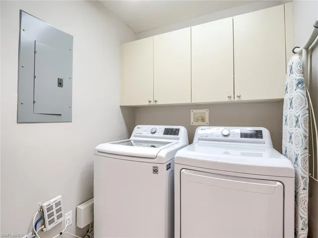 Clothes washing area with cabinets, electric panel, and separate washer and dryer