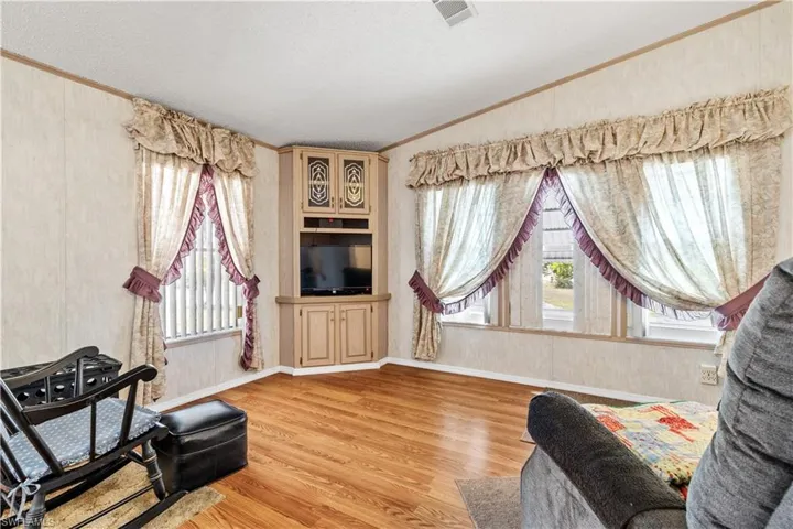 Living area with vaulted ceiling, crown molding, light wood-style floors, and plenty of natural light