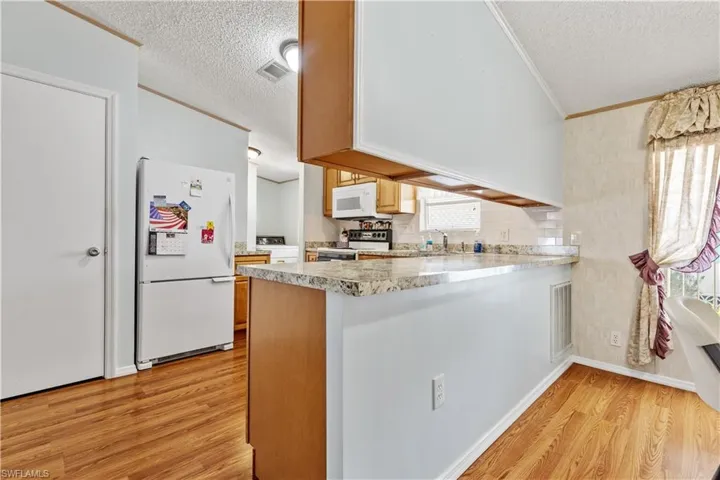 Kitchen featuring white appliances, a textured ceiling, ornamental molding, light wood-style floors, and light stone countertops