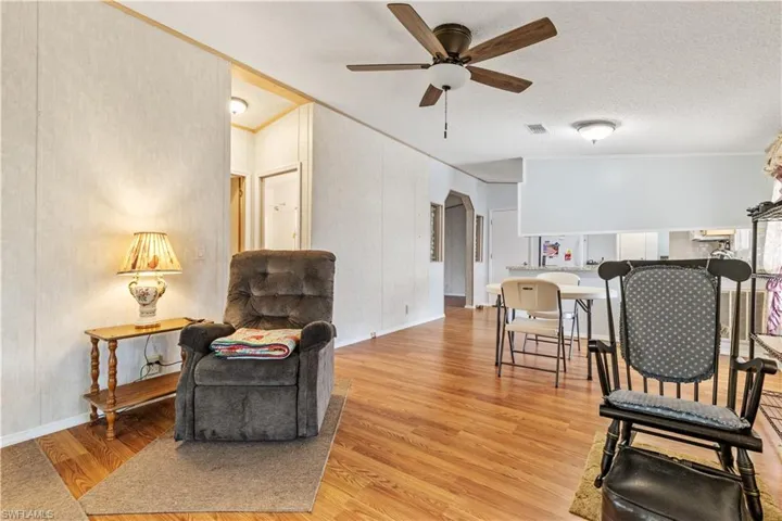 Living area featuring ceiling fan, ornamental molding, light wood-style floors, a textured ceiling, and arched walkways