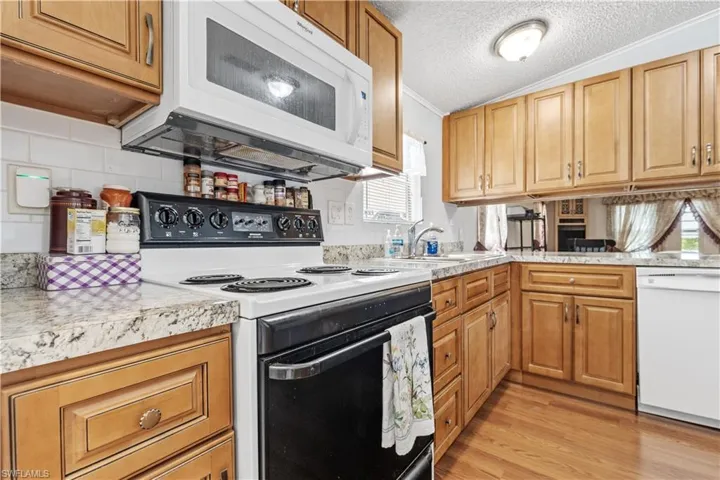 Kitchen featuring white appliances, a textured ceiling, light wood finished floors, wood finish cabinets, and crown molding