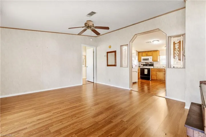 Unfurnished living room with light wood-style floors, a ceiling fan, arched walkways, crown molding, and a textured ceiling