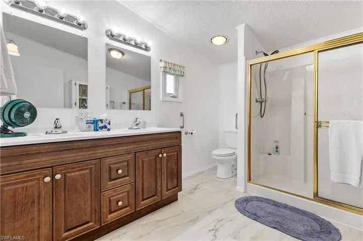 Bathroom featuring a shower stall, double vanity, a textured ceiling, and light marble finish floors