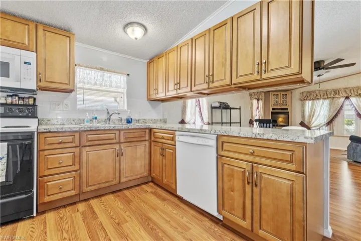 Kitchen with white appliances, a textured ceiling, light wood-type flooring, a ceiling fan, and ornamental molding