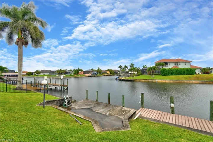Waterfront property featuring a private boat ramp, wooden dock, mature palm trees, and manicured lawn