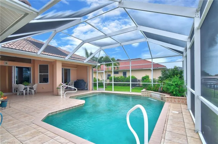 Screened-in pool enclosure featuring a geometric pool with a waterfall element