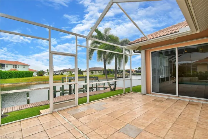Screened lanai featuring large format tile flooring, a waterside dock, and a sliding glass door entry to the interior