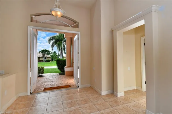Double entry doors with an arched transom, a decorative chandelier, and tile flooring throughout