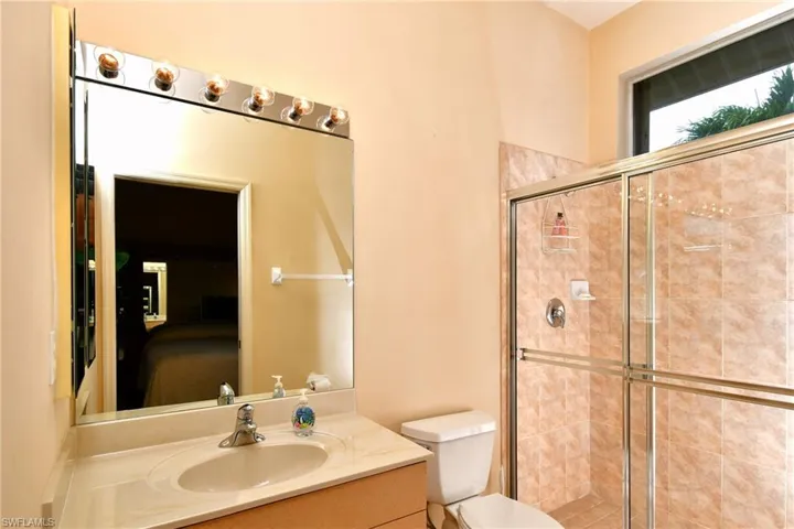 Bathroom featuring a light-toned vanity with an integrated sink and countertop, a frameless wall mirror, and a shower enclosure with a sliding glass door and tile surround