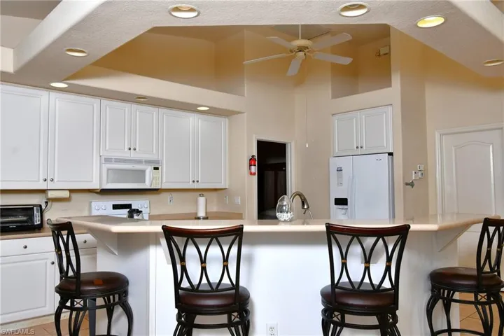 Kitchen featuring a breakfast bar with seating, white cabinetry, recessed lighting, and a vaulted ceiling with a ceiling fan